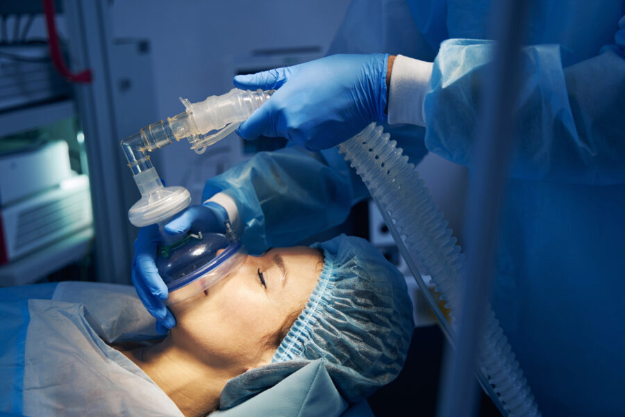 Anesthesia provider administering general anesthesia with a ventilation mask in a hospital surgical setting.