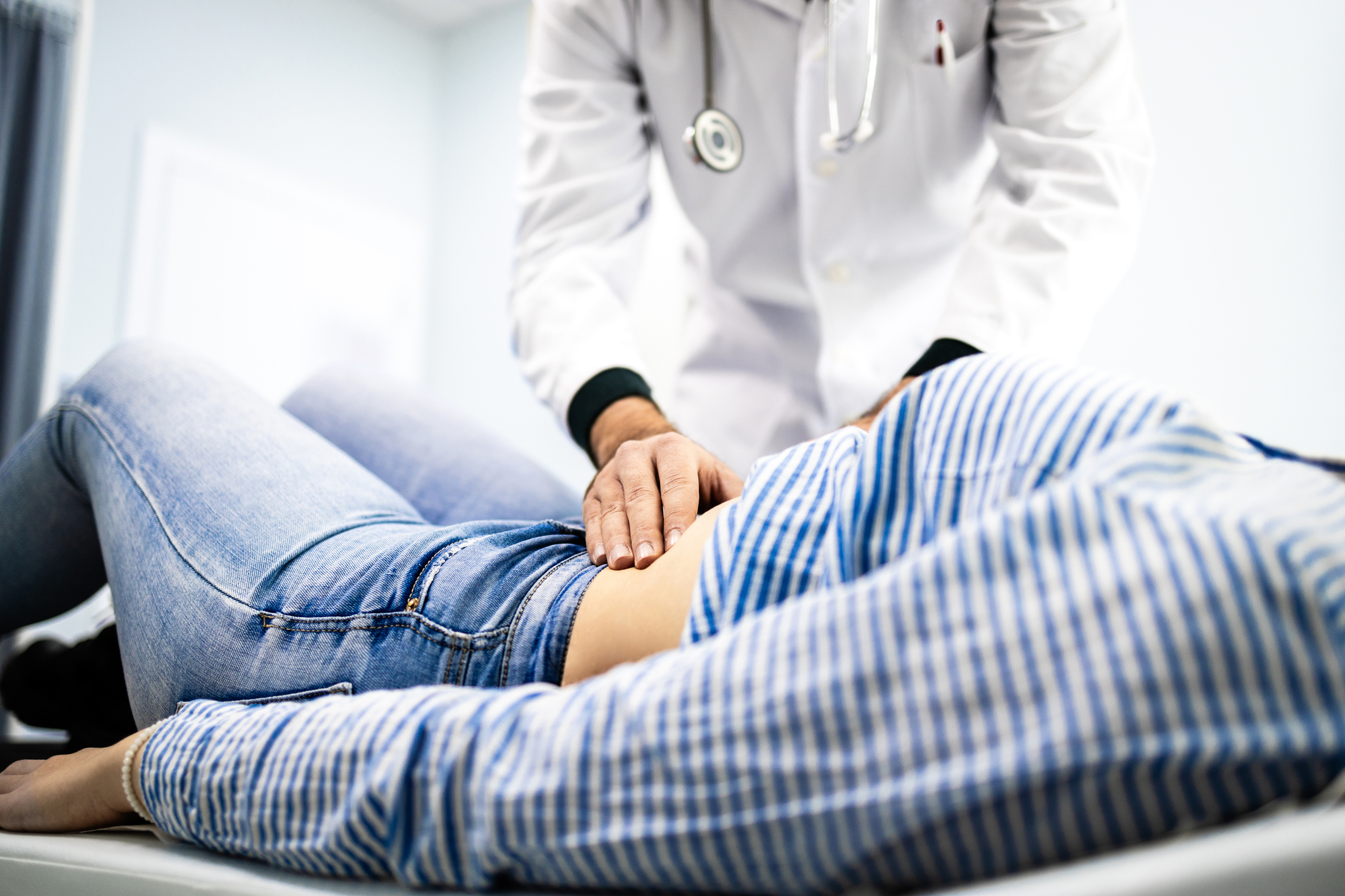 Gastroenterologist performing an abdominal examination on a patient lying on an exam table, assessing for gastrointestinal issues.