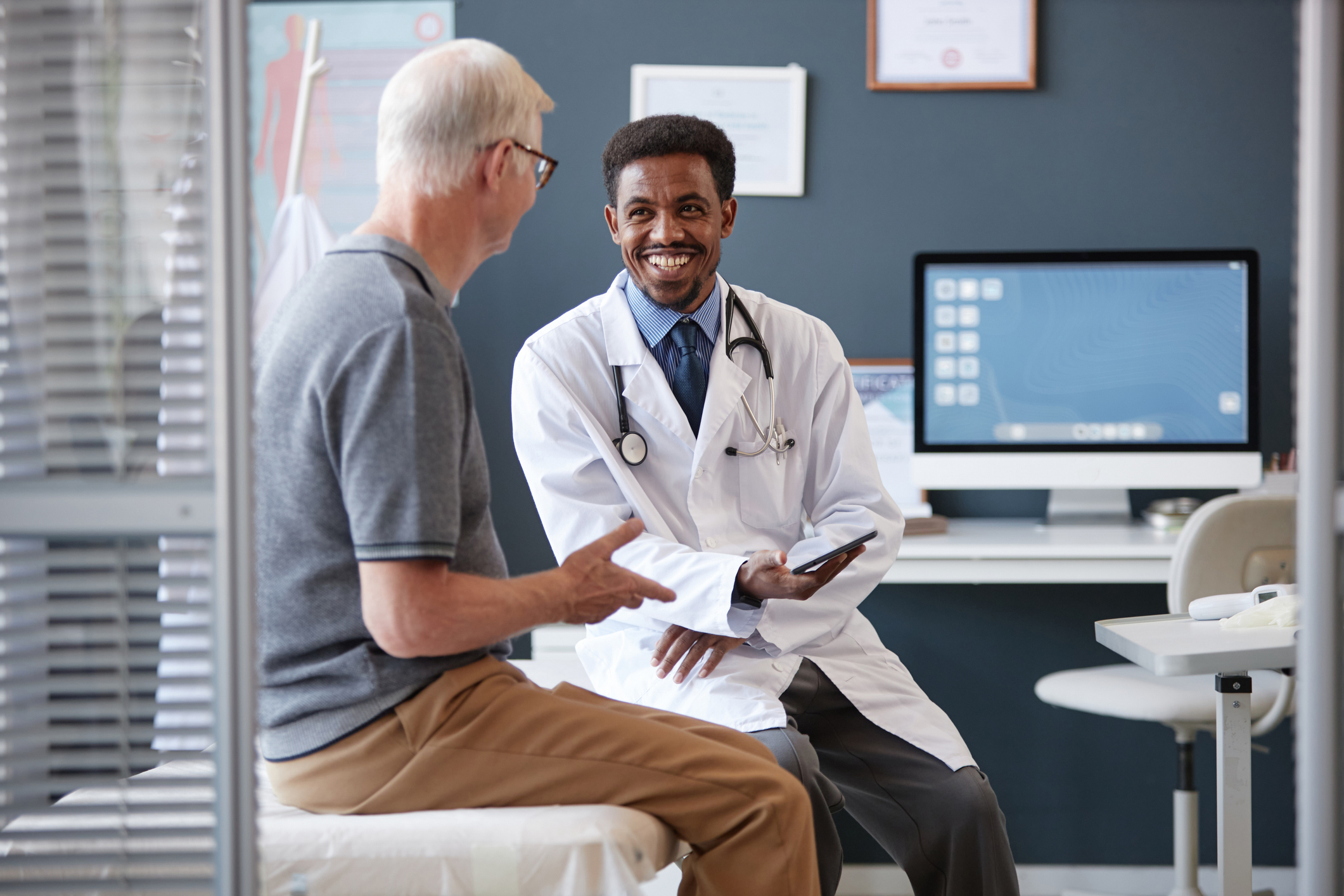 Primary care physician speaking with an older male patient during a consultation in a medical office setting.